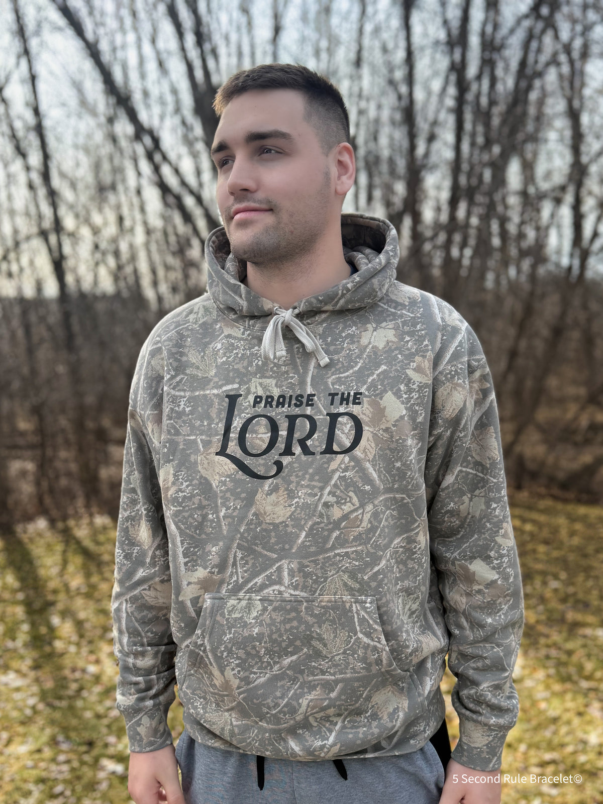 Person wearing a camouflage hoodie with 'Praise the Lord' text outdoors.