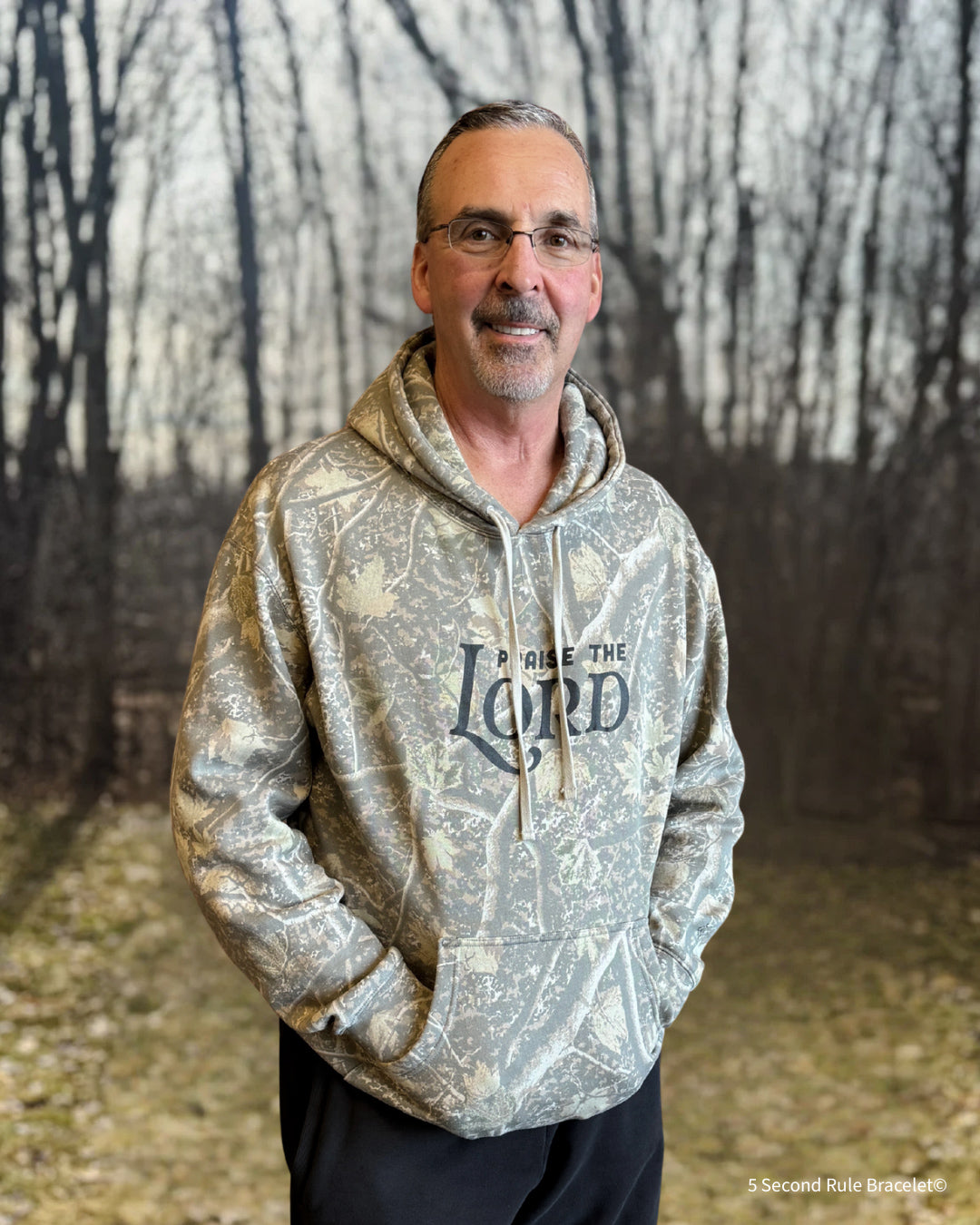 Man wearing a hoodie with text standing in front of a forest background