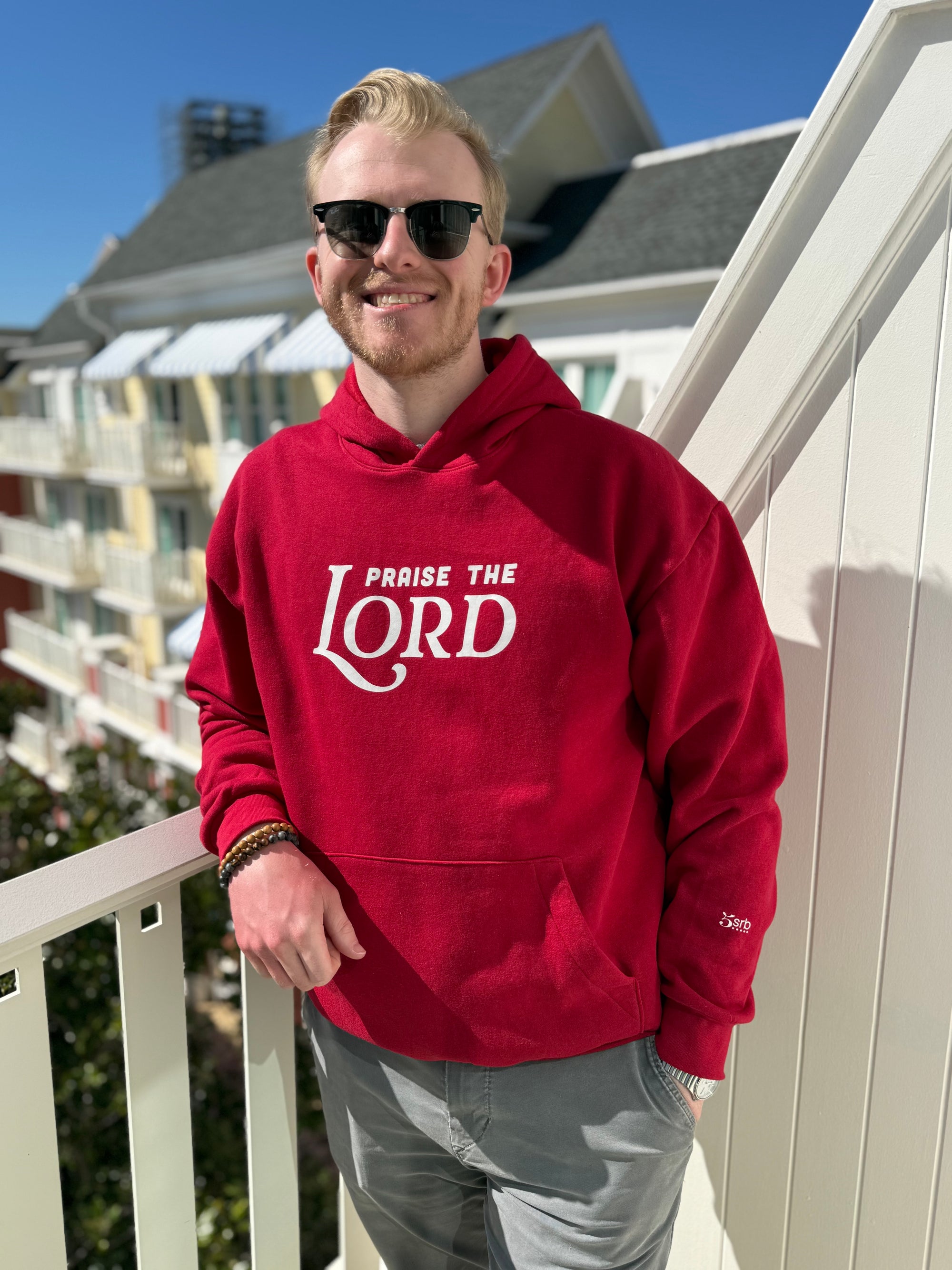Man wearing a red hoodie with 'PRAISE THE LORD' text on a balcony.