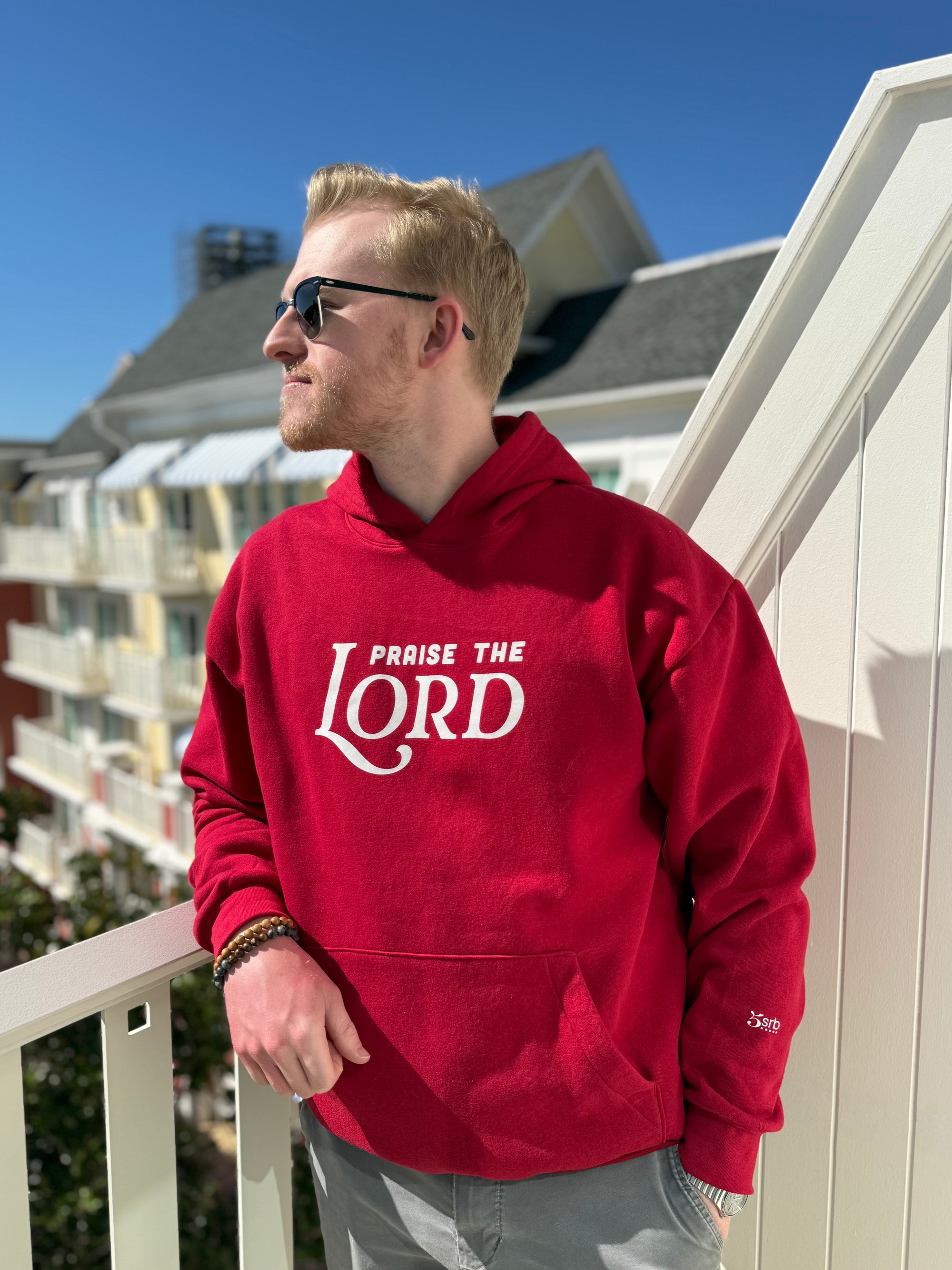 Man wearing a red hoodie with 'Praise the Lord' text on a balcony.
