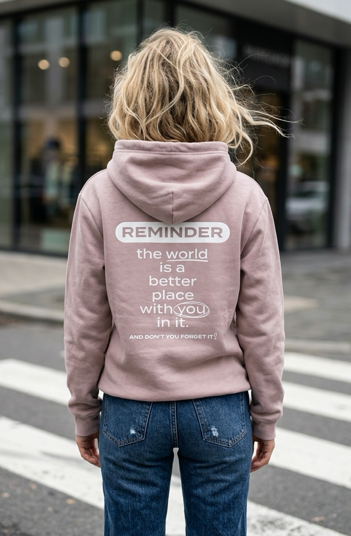Person wearing a pink hoodie with a motivational quote on the back, standing on a crosswalk.
