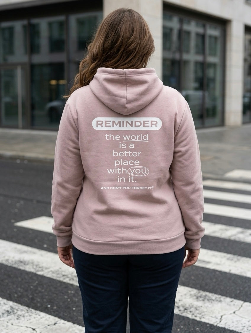 Person wearing a pink hoodie with a motivational message on the back, standing on a street.