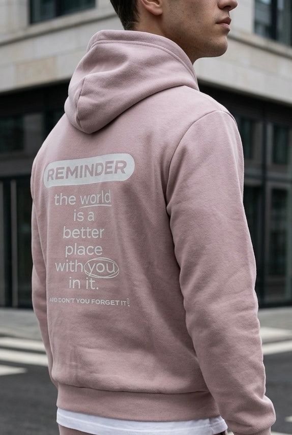 Person wearing a pink hoodie with a motivational message on the back, standing in an urban setting.