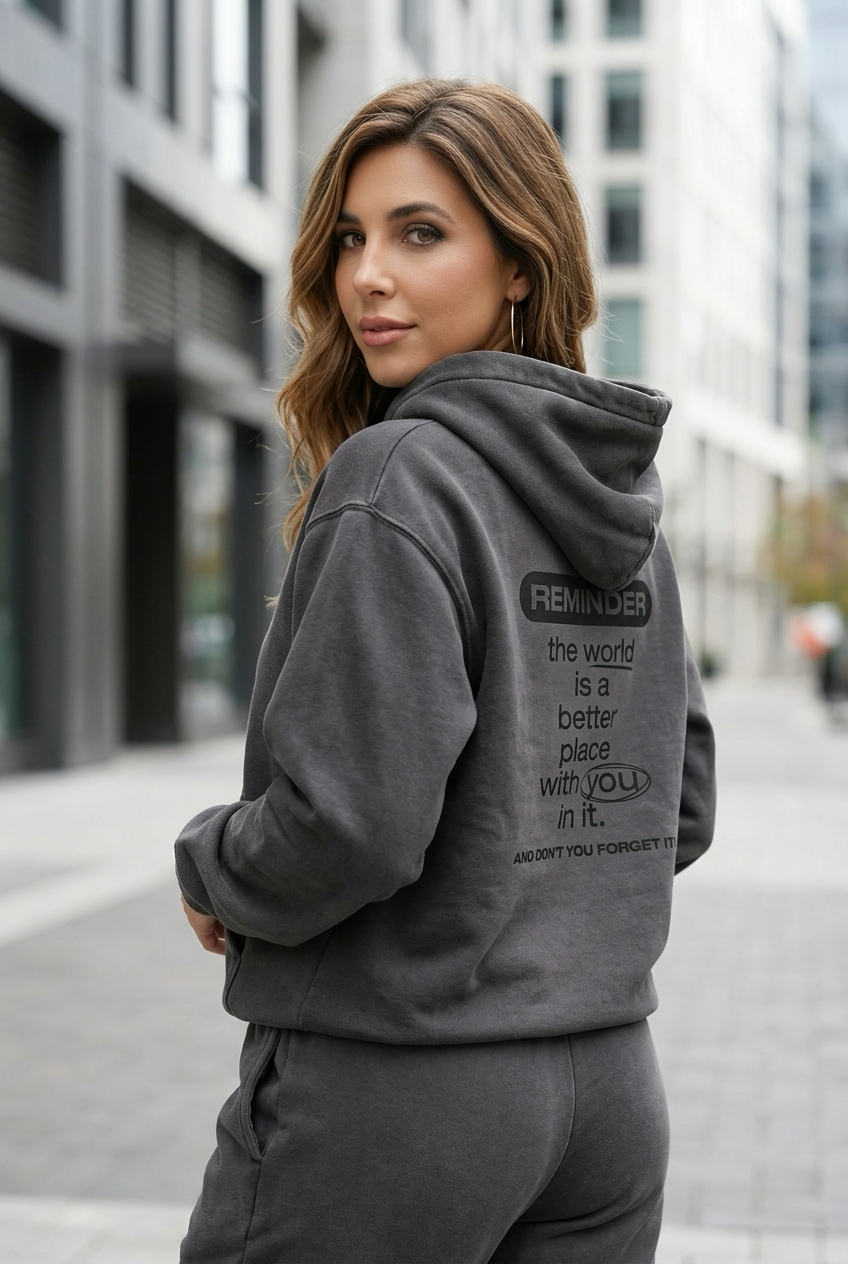 Woman wearing a gray hoodie with text on the back in an urban setting