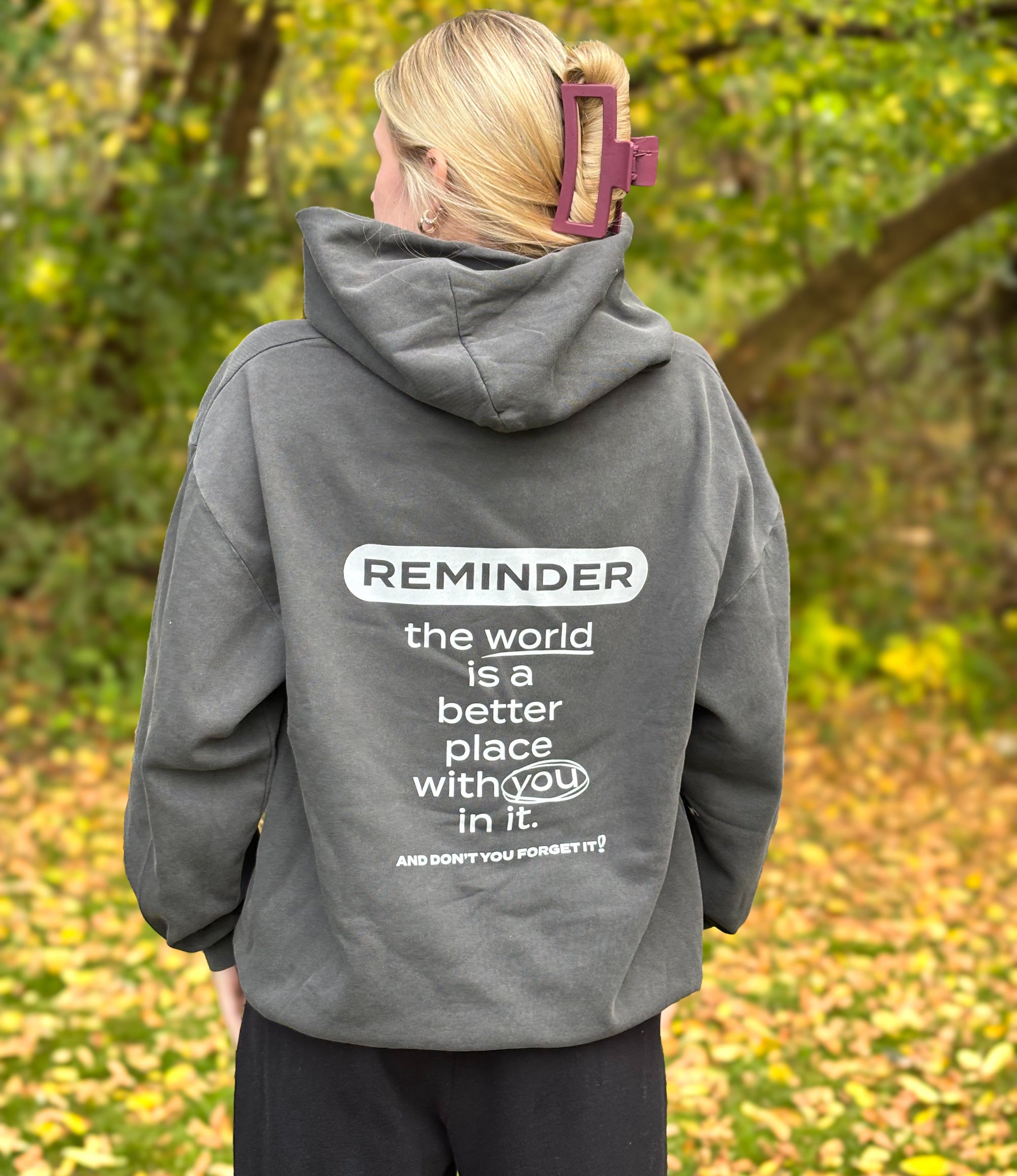 Person wearing a gray hoodie with a motivational message on the back, standing in a forest.