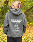 Person wearing a gray hoodie with a motivational message on the back, standing in a forest.
