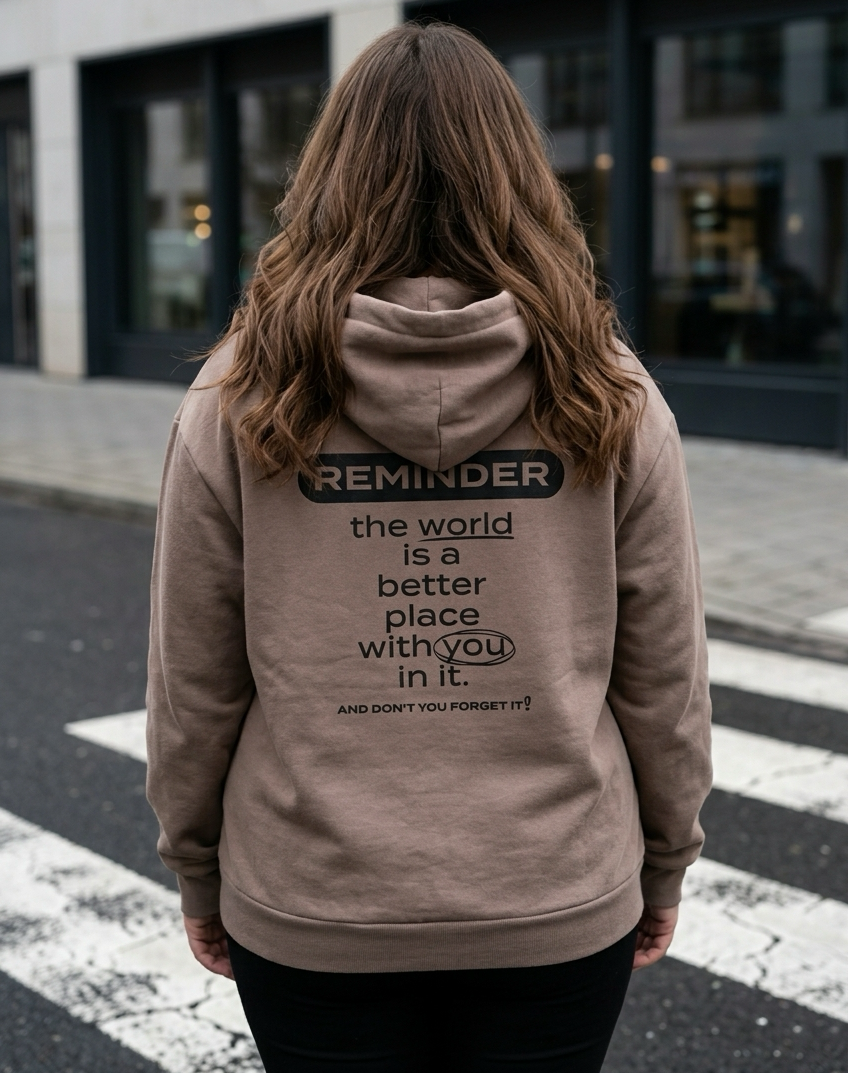 Person wearing a hoodie with a motivational message on the back, standing on a street.