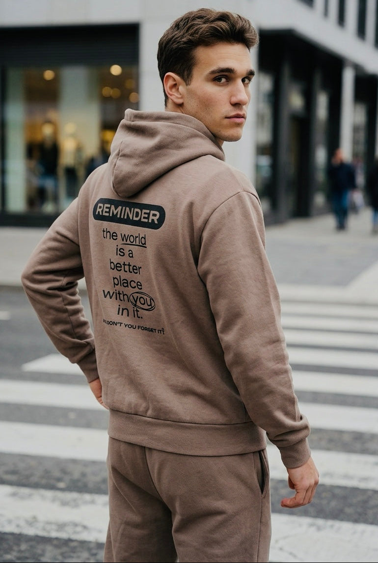 Man wearing a beige hoodie with a motivational message on the back, standing on a city street.