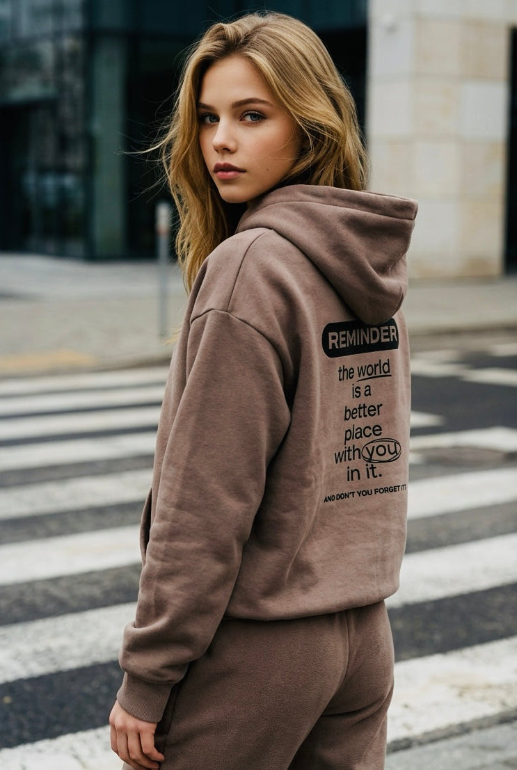 Woman wearing a brown hoodie with text on the back, standing on a crosswalk.