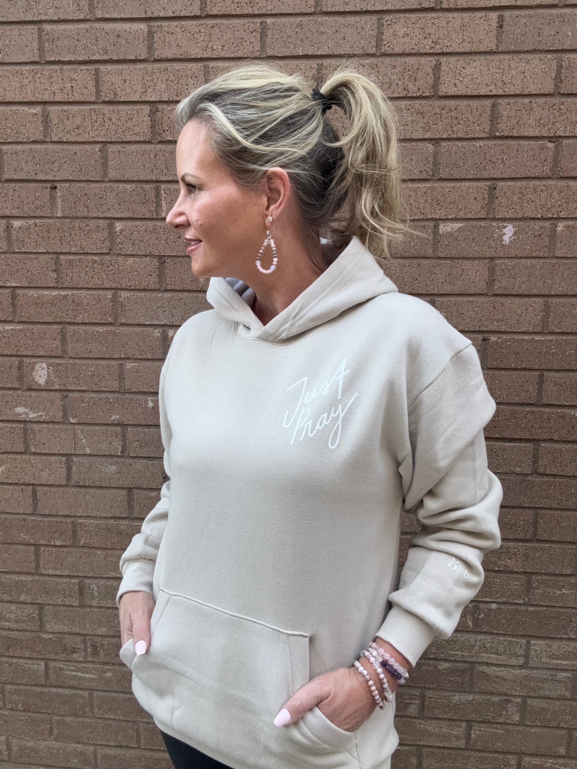 Person wearing a light tan hoodie with text on a brick pavement