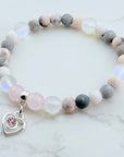 Beaded bracelet with a heart charm featuring a pink gemstone on a marble surface