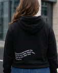 Person wearing a black hoodie with text on the back, standing outdoors.