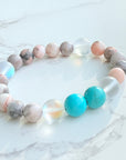 A bracelet with round beads in shades of turquoise, pink, white, and gray, displayed on a marble surface.
