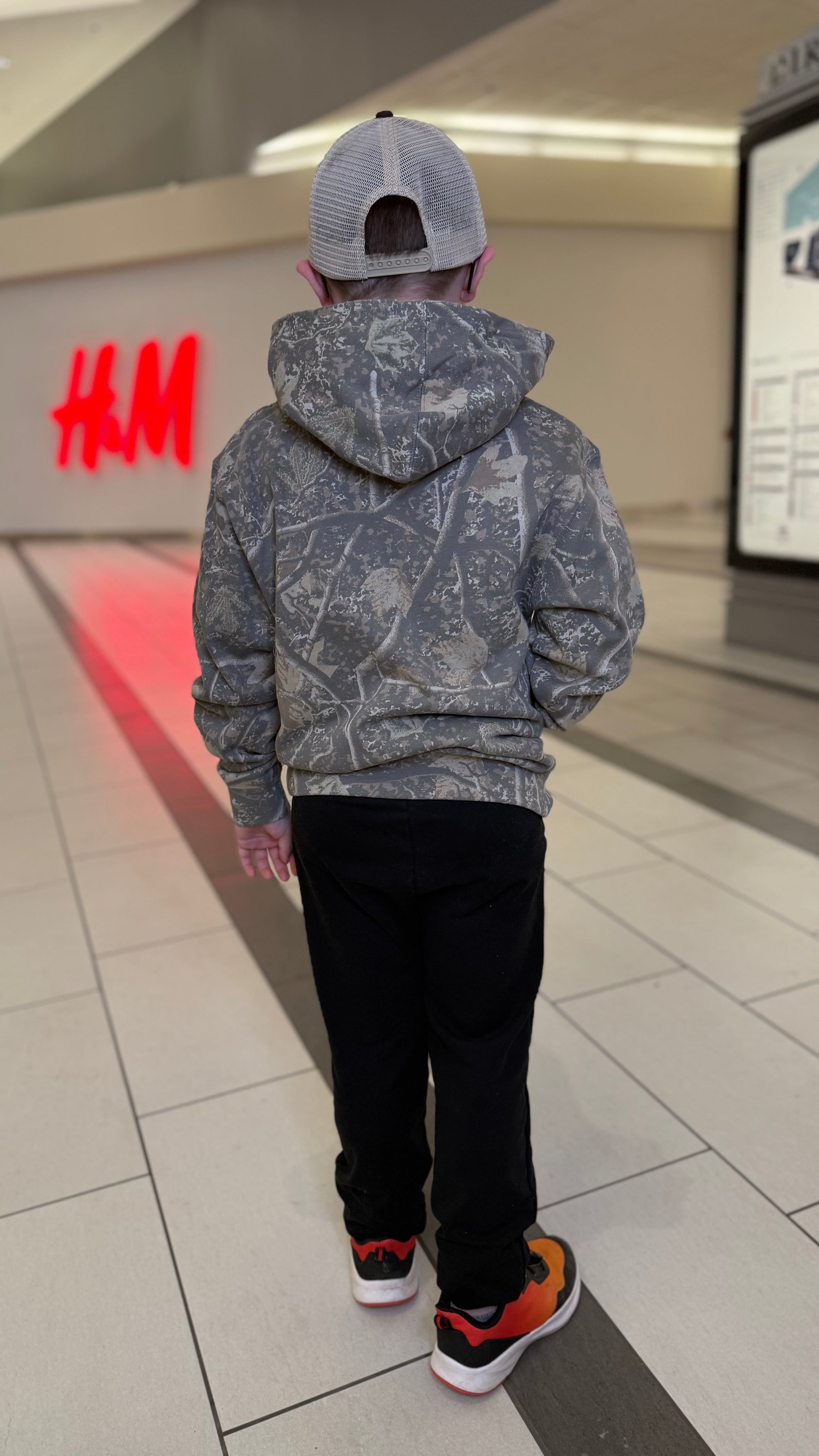 Person wearing a gray hoodie and black pants standing in a store with an H&M logo in the background.
