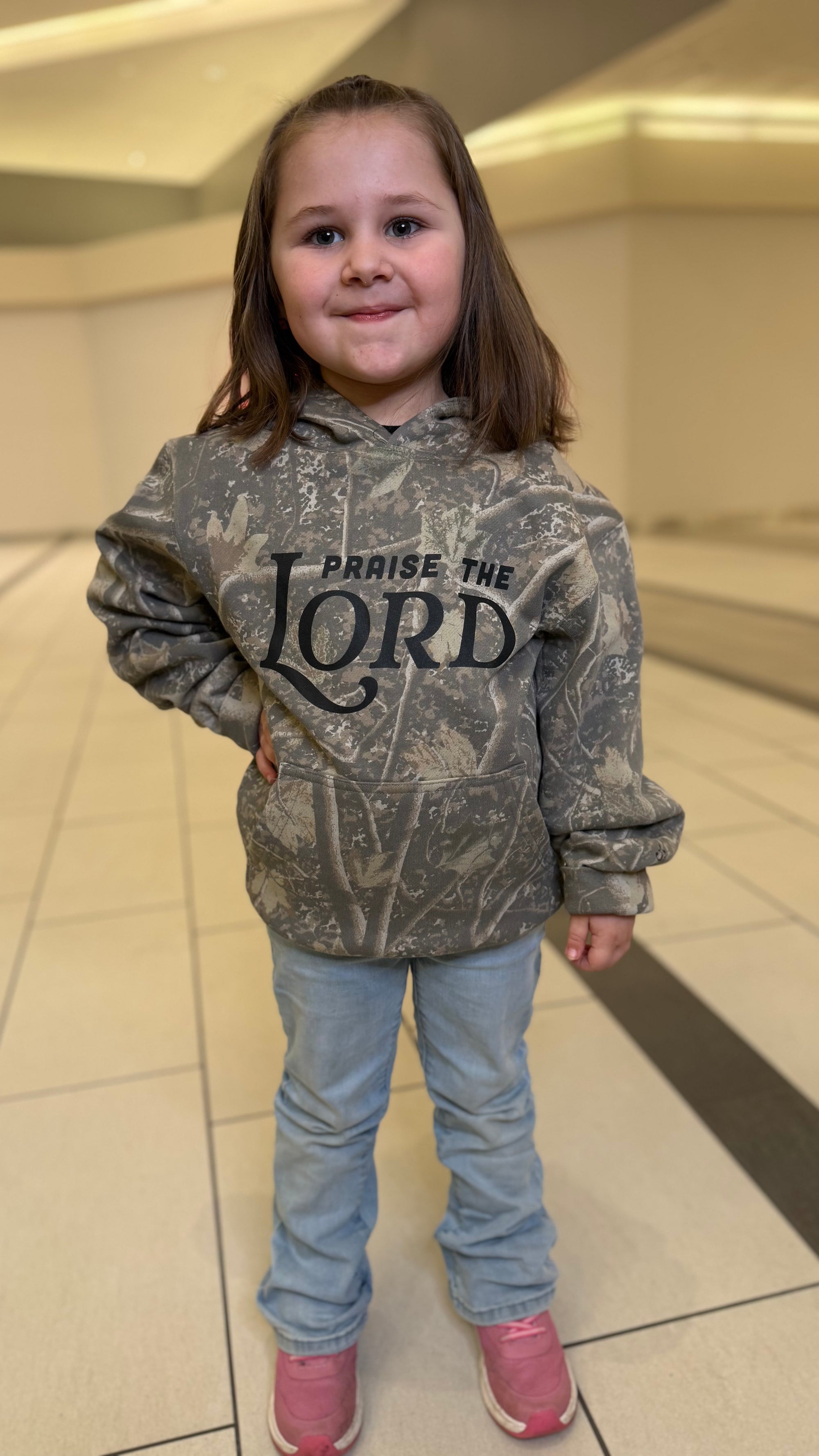 Child wearing a hoodie with 'Praise the Lord' text in a hallway.