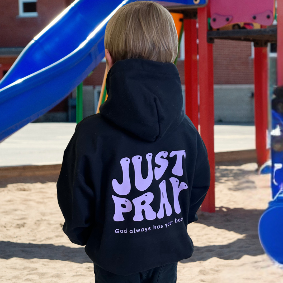 Child wearing a black hoodie with &#39;JUST PRAY&#39; text at a playground