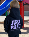 Child wearing a black hoodie with 'JUST PRAY' text at a playground