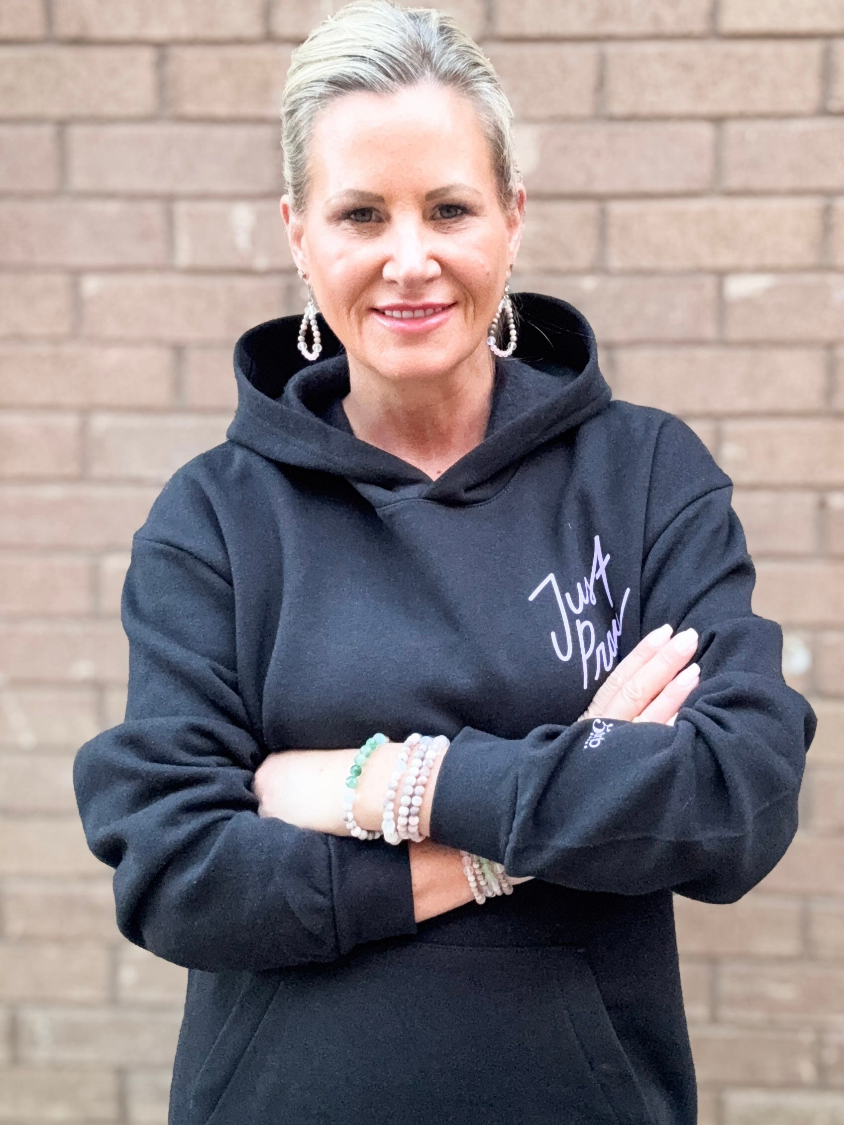 Woman wearing a black hoodie with text, standing against a brick wall.