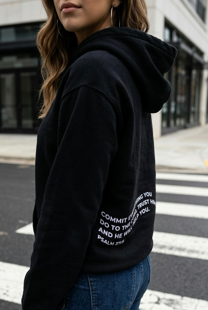 Person wearing a black hoodie with text on the back, standing on a street.