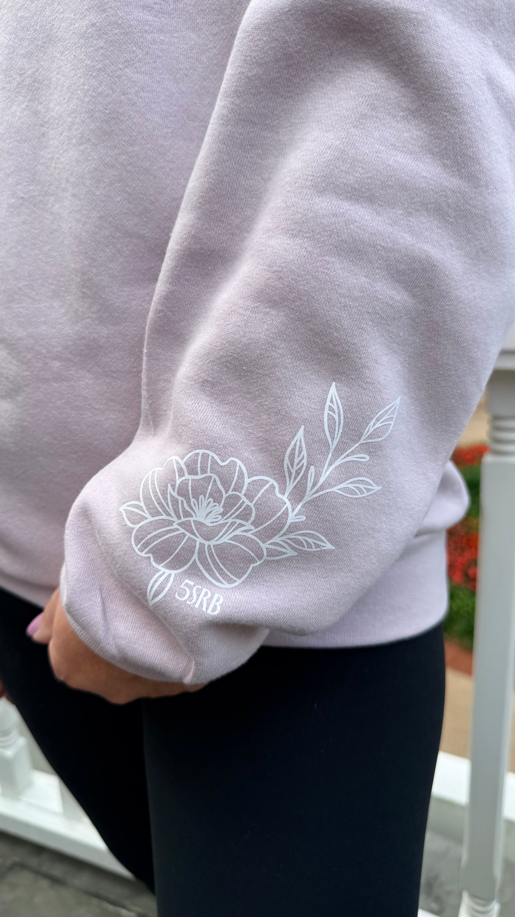 Close-up of a blush sweatshirt with white floral embroidery on a blurred background