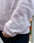 Close-up of a blush sweatshirt with white floral embroidery on a blurred background
