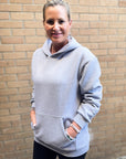 Woman wearing a gray hoodie standing against a brick wall
