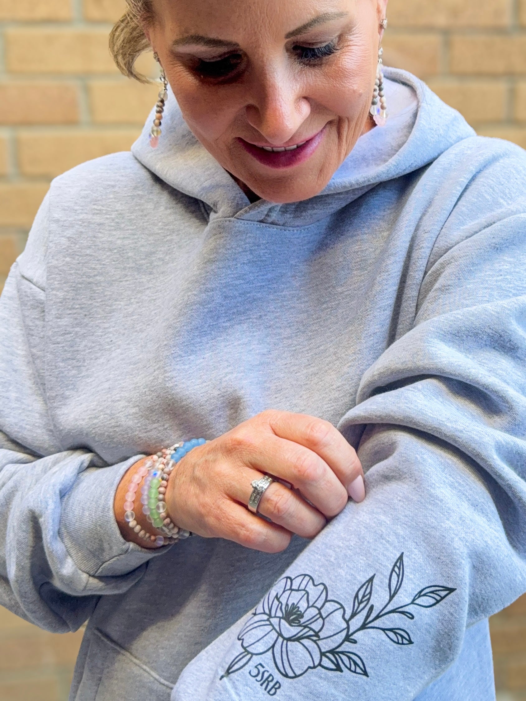 Person wearing a gray hoodie with a floral design and initials on a brick wall background