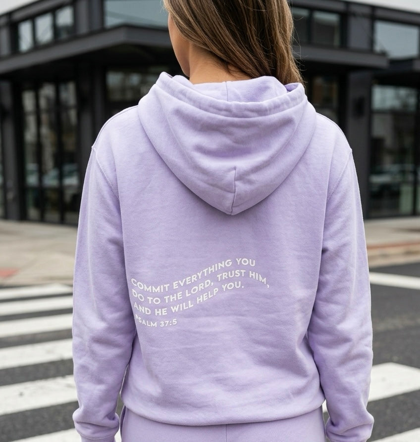 Person wearing a lavender hoodie with text on the back, standing outdoors.
