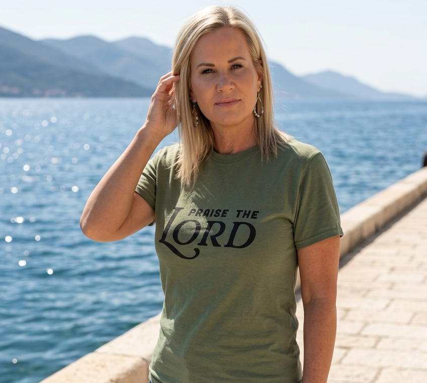 Woman wearing a green t-shirt with 'Praise the Lord' text by a body of water.