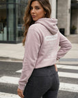 Woman wearing a light pink hoodie with text on it, standing on a street.