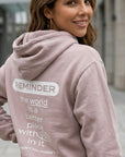 Woman wearing a hoodie with a motivational message on the back, standing outdoors.