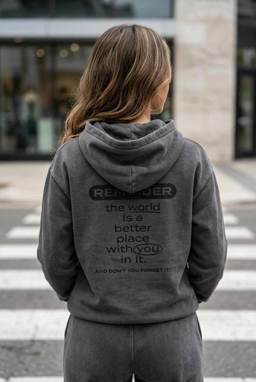 Person wearing a gray hoodie with a motivational message on the back, standing on a crosswalk.