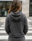 Person wearing a gray hoodie with a motivational message on the back, standing on a crosswalk.