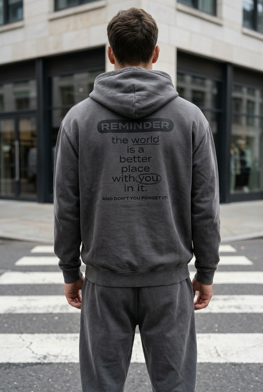 Person wearing a gray hoodie with a motivational message on the back, standing on a city street.