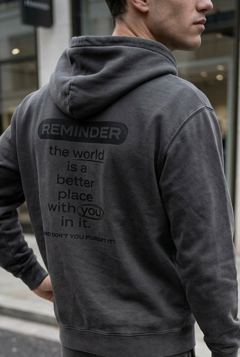 Person wearing a gray hoodie with a motivational message on the back, standing in an urban setting.