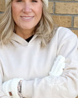 Person wearing a white beanie, white hoodie, and white gloves standing against a brick wall.