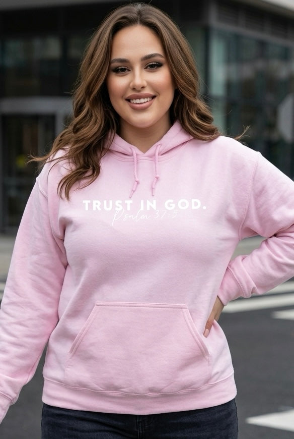Person wearing a pink hoodie with 'TRUST IN GOD' text outdoors.