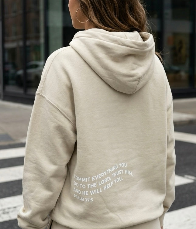 Person wearing a beige hoodie with text on the back, standing on a street.