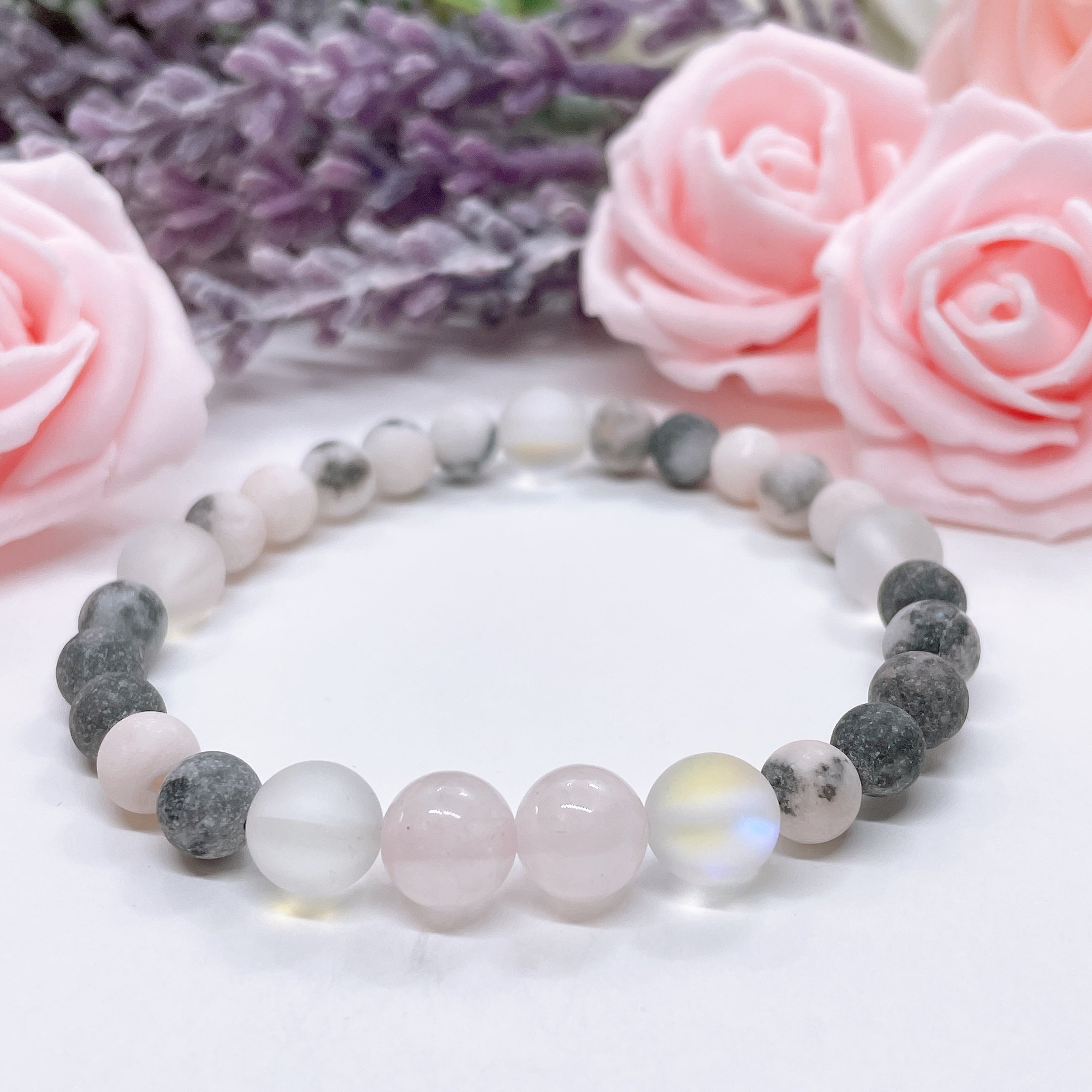 The Rose Quartz Companion Gemstone stretch bracelet made with 2 pink rose quartz gemstones, translucent aura beads, and pink jasper gemstones sit on a white table.