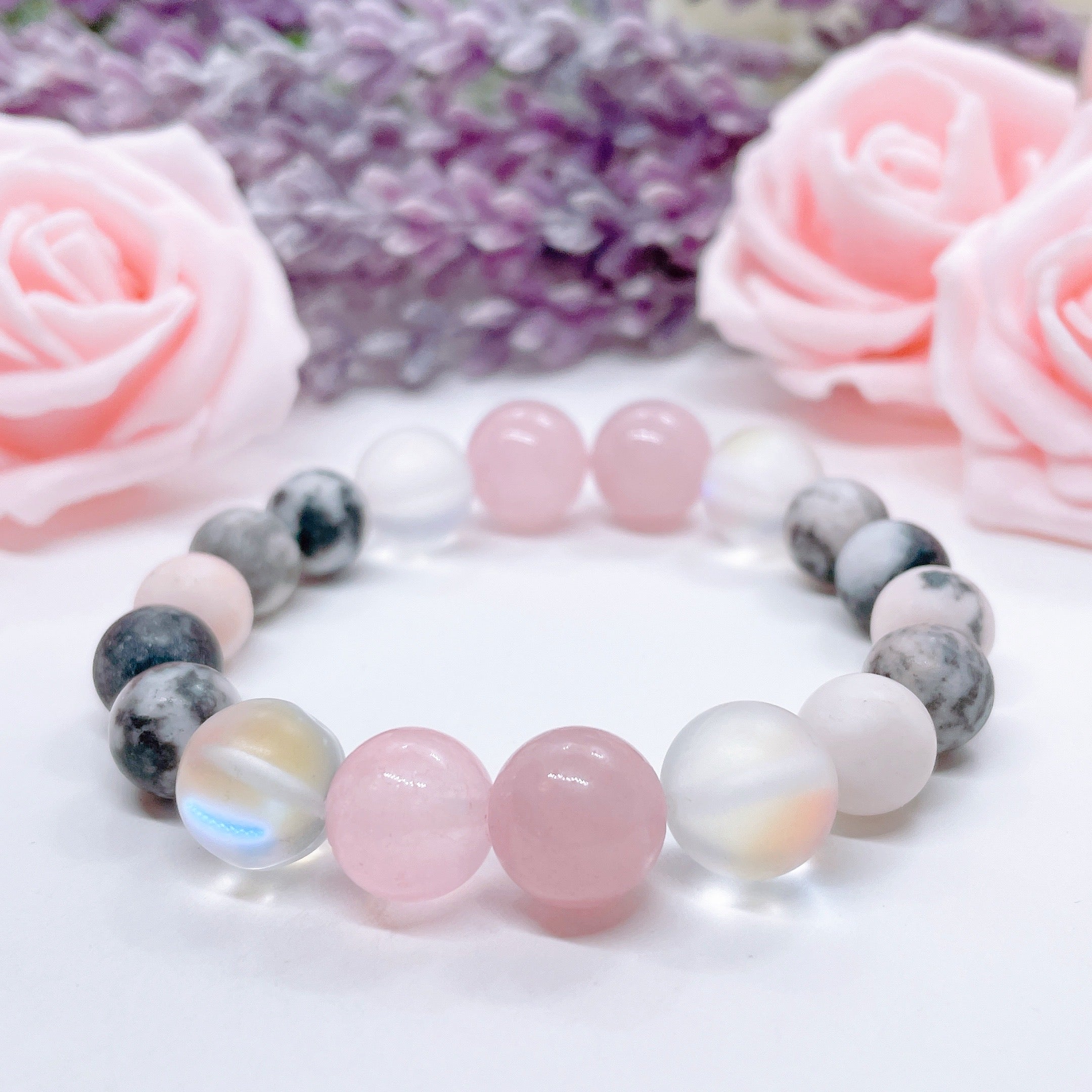 A Rose Quartz Gemstone stretch bracelet made with 2 pink rose quartz gemstones, translucent aura beads, and pink jasper gemstones sit on a white table. 