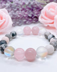 A Rose Quartz Gemstone stretch bracelet made with 2 pink rose quartz gemstones, translucent aura beads, and pink jasper gemstones sit on a white table. 