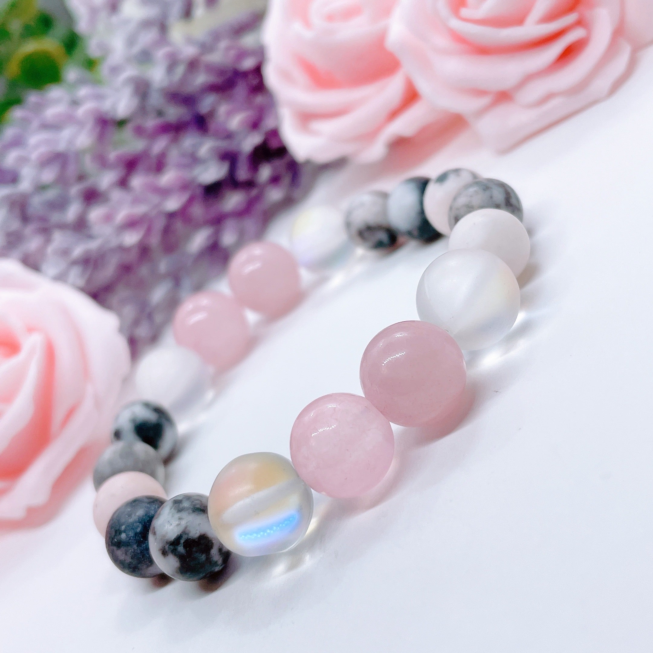 A Rose Quartz Gemstone stretch bracelet made with 2 pink rose quartz gemstones, translucent aura beads, and pink jasper gemstones sit on a white table. 