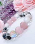 A Rose Quartz Gemstone stretch bracelet made with 2 pink rose quartz gemstones, translucent aura beads, and pink jasper gemstones sit on a white table. 