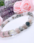 A Rose Quartz Rhinestone Companion Gemstone stretch bracelet made with 4 pink rose quartz gemstones, translucent aura beads, pink jasper gemstones, and rhinestone accents for added sparkle sits on a white table. 