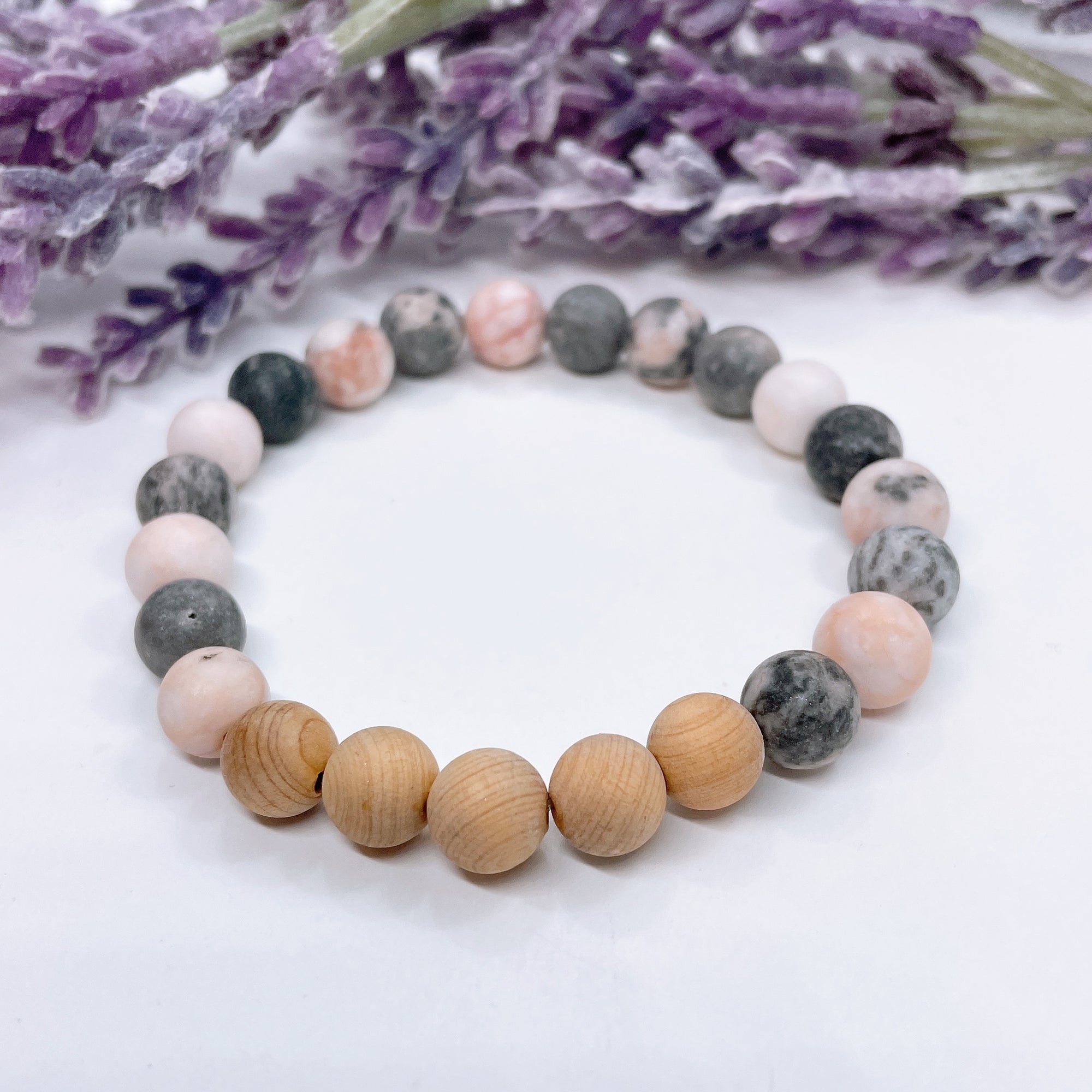 A Pink Zebra Jasper and Cedar Wood gemstone stretch bracelet sits on a white table.